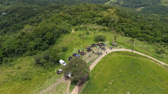 Vista aérea de grupo e UTVs reunidos em uma trilha cercada por vegetação.