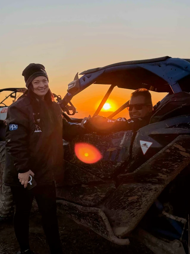 Participantes ao lado de um UTV durante o pôr do sol.